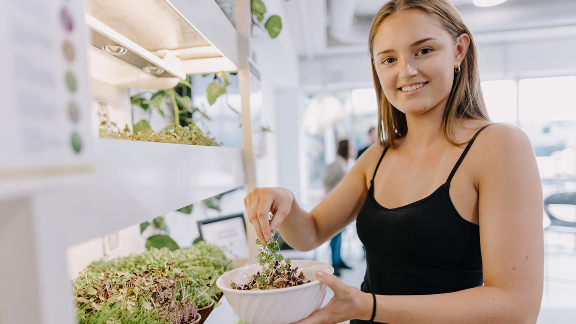 Person smiling while adding freshly harvested microgreens to a bowl at a Farmwall